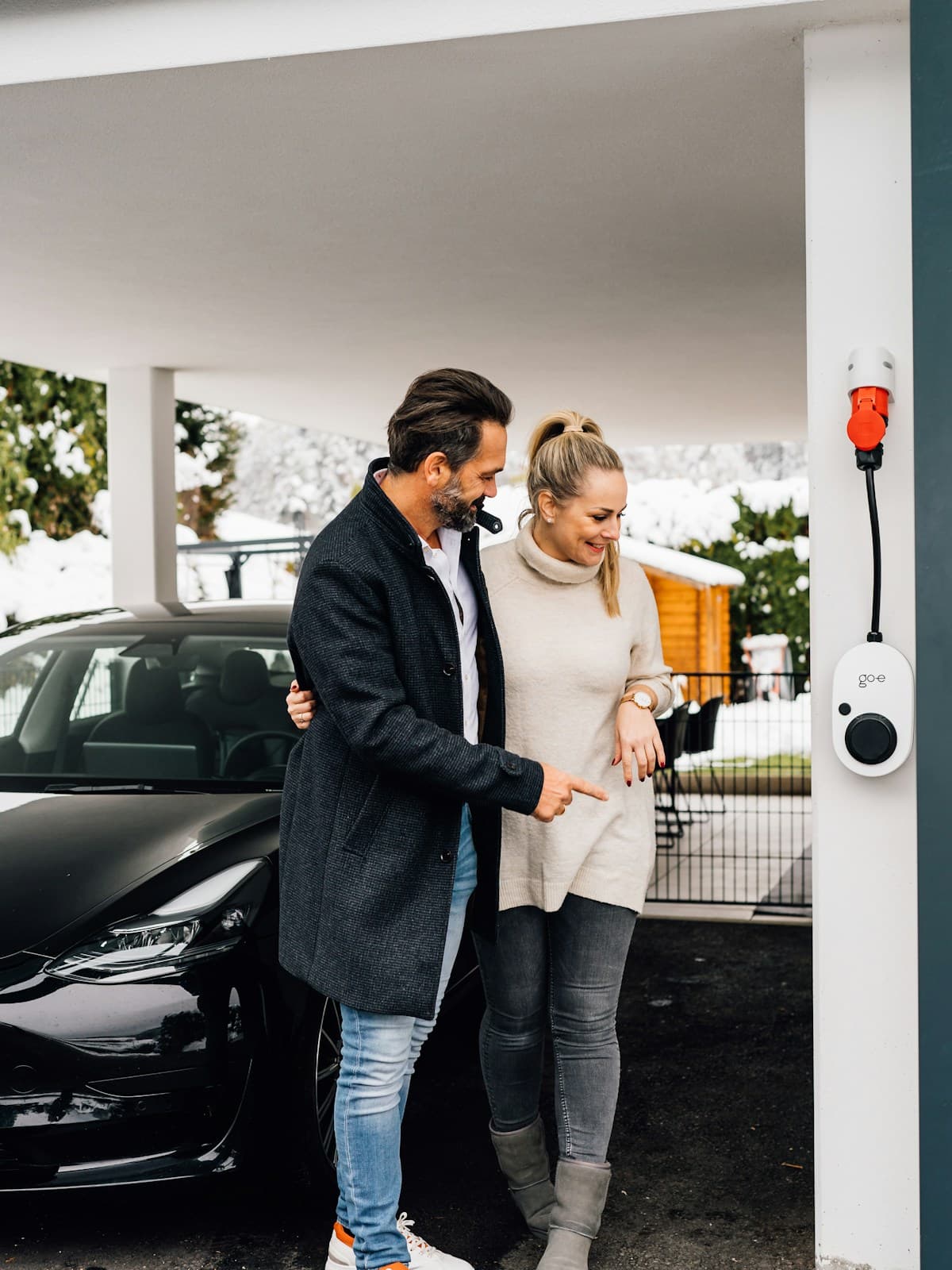 Couple smiling beside their electric vehicle at a charging station